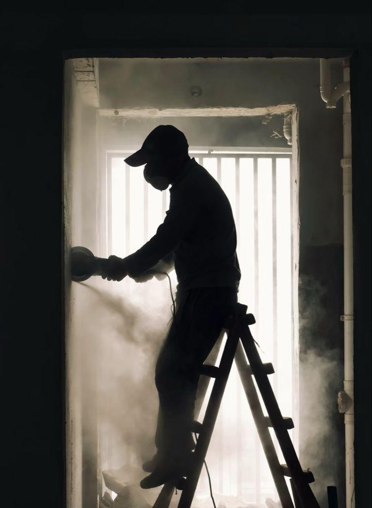 Contractor grinding a wall during a renovation, backlit by dust and light
